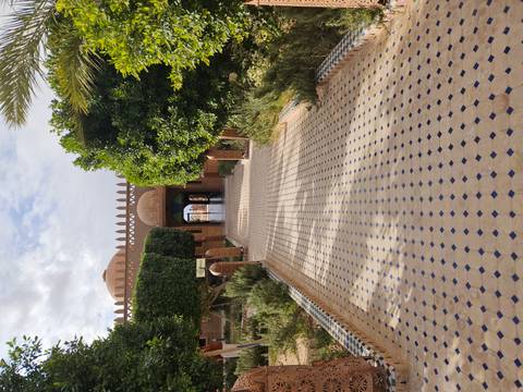 Pathway leading to a Moroccan building surrounded by gardens.