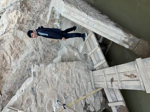 Person navigating makeshift wooden bridge over a small body of water.
