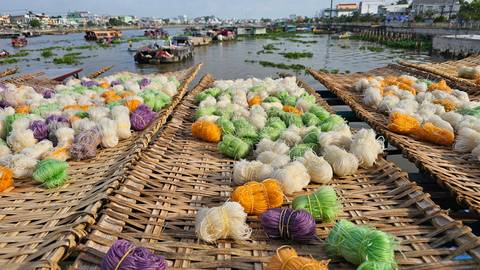 Colorful bundles of thread drying by the riverbank with boats nearby.