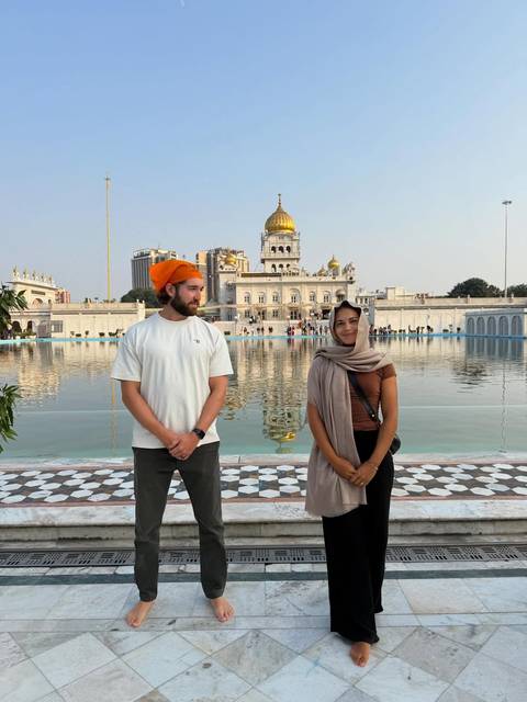 Two people standing in front of a gurudwara with a water body.