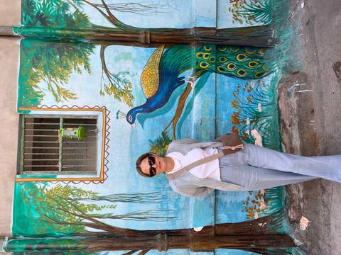 Woman posing in front of a peacock mural on a wall.