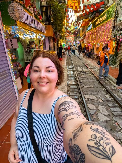 A person taking a selfie near railway tracks with people walking.