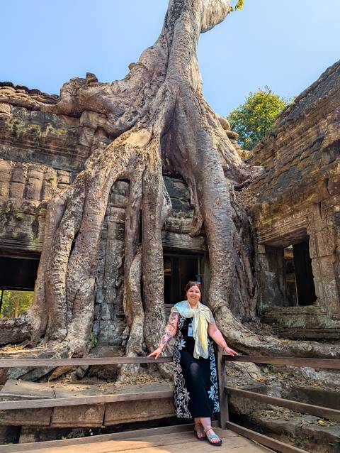 A person posing near an ancient tree and ruins at a temple.