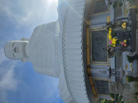 Large white statue of Buddha with lotus base and offering table below.