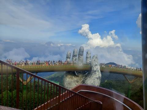 Golden Bridge with large hand sculptures and clouds in the background.