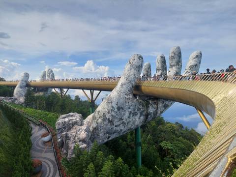 Golden Bridge with giant hands supporting it, surrounded by greenery.