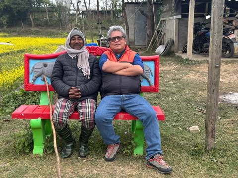 Two men sitting on a colorful bench, outside in a rural area.