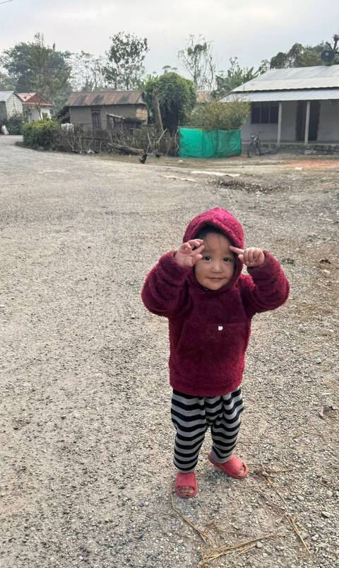 A young child in a red sweater standing outdoors on a gravel surface.