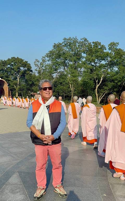 A man standing among monks in traditional attire, in a pathway surrounded by trees.
