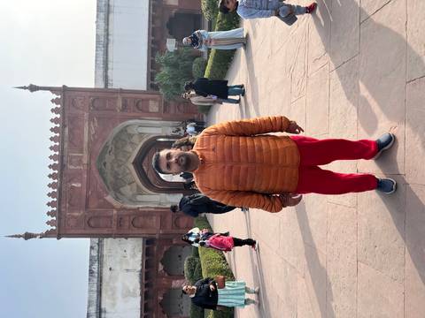Person standing in front of a historic red stone building with an archway.