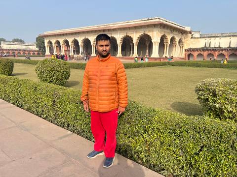 Person standing in a garden with historic architecture in the background.