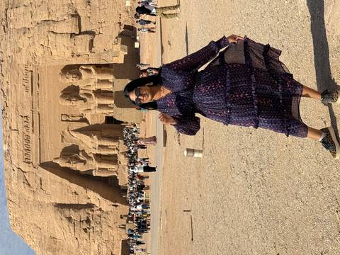 Tourist posing in front of Abu Simbel temple, with large statues carved into the rock.