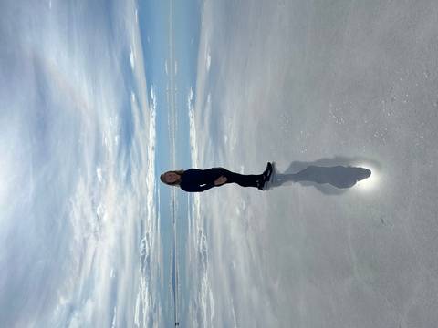 A woman standing on reflective salt flats with the sky reflected in the water.