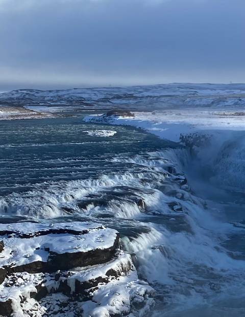 A powerful waterfall cascading into a river surrounded by snowy banks.
