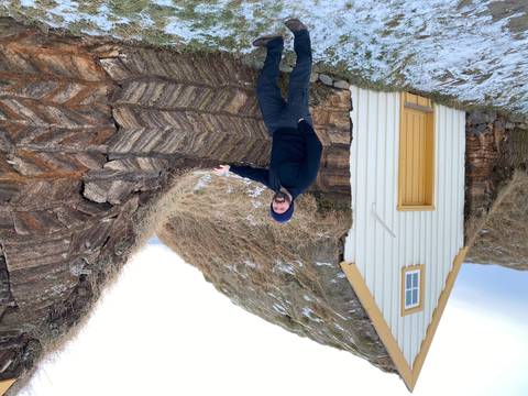 Person standing beside a traditional turf house in a snowy setting.