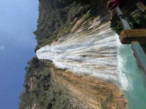 Tall waterfall cascading down a rocky cliff with trees nearby.