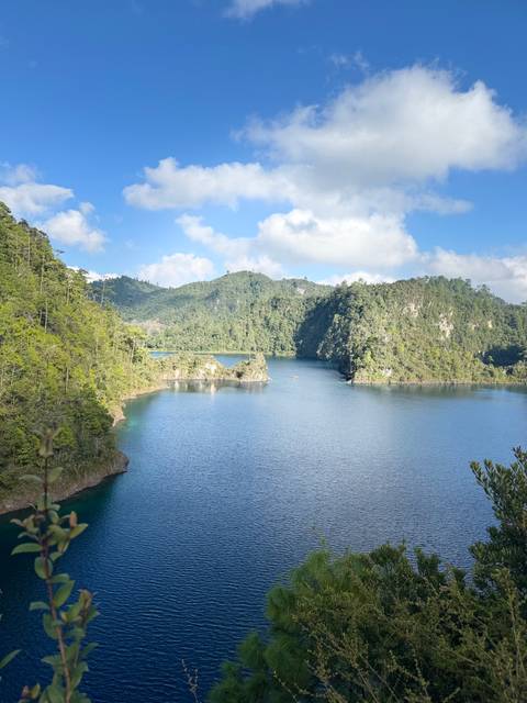 Serene lake view with green hills in the background under a bright sky.