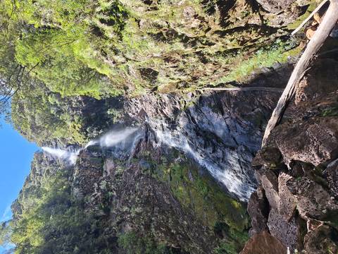 Tall waterfall amidst rocky cliffs and greenery.
