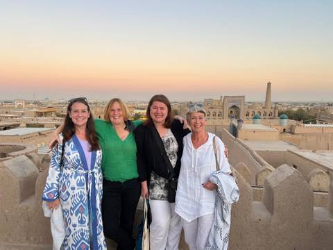 Group of women standing on a rooftop with a historic city view at sunset.