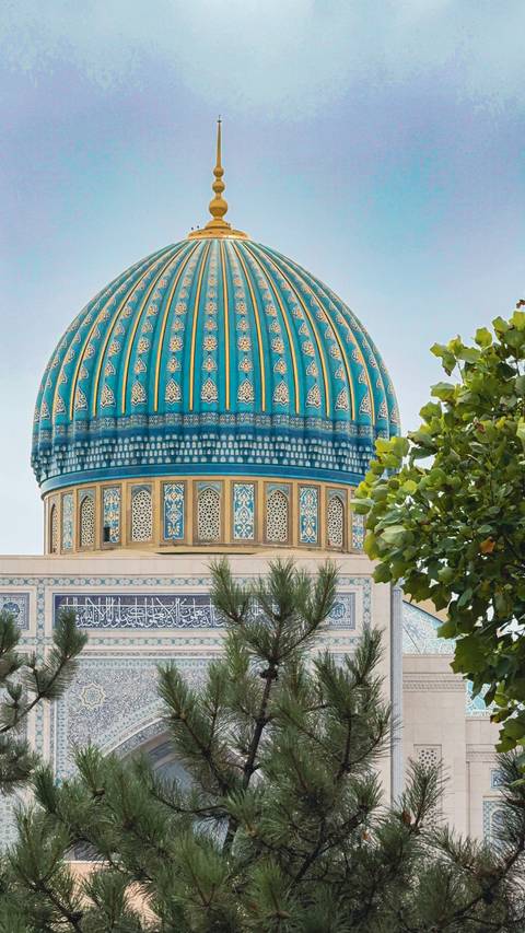 Close-up of a blue-tiled dome with intricate designs and trees nearby.