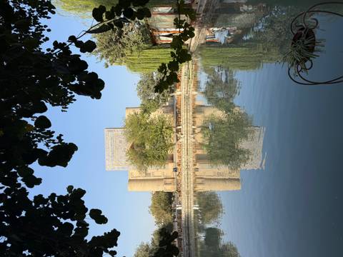 Scenic view of a historic building reflected in a pond surrounded by trees.