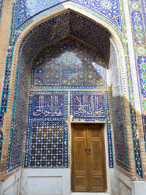 Close-up of an ornate blue-tiled facade with Arabic script and vibrant patterns.