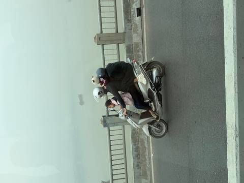 Family riding a scooter on a bridge in foggy weather.