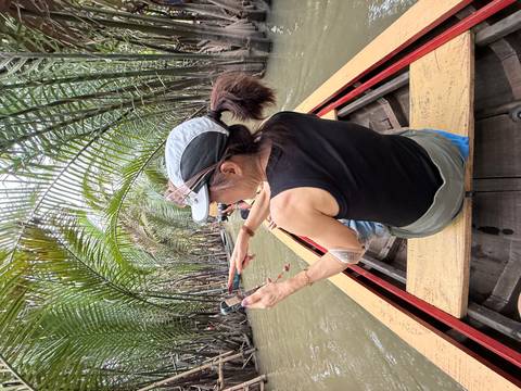 Woman photographing in a boat through waterway surrounded by trees.