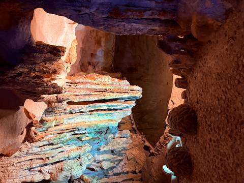 Colorful cave interior with stalactites and small pool.