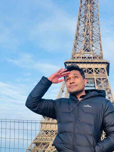 Person saluting with the Eiffel Tower in the background.