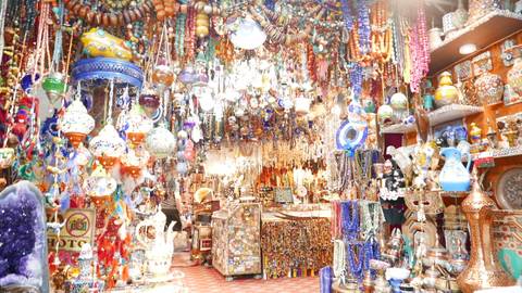 Brightly lit bazaar packed floor-to-ceiling with hanging glass lamps, beads and ceramics, creating a colourful overload.