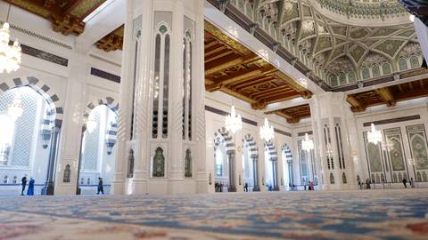 Opulent prayer hall of the Sultan Qaboos Grand Mosque with soaring white marble columns, patterned arches and sparkling chandeliers.