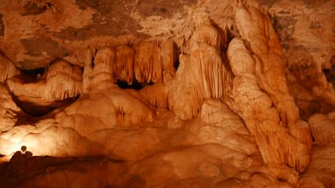Orange-lit cave chamber with flowstone formations and a seated visitor silhouetted in the corner.