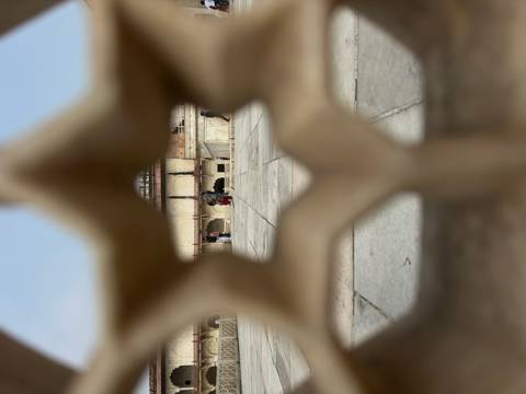 Creative shot through a star-shaped lattice focusing on visitors inside a historic courtyard.