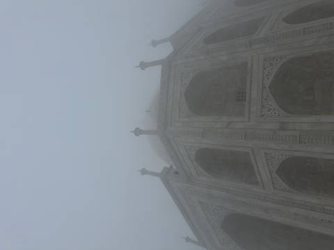Taj Mahal shrouded in thick morning fog, its marble silhouette barely visible.