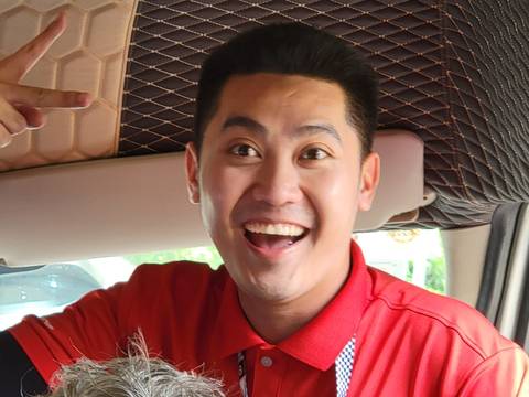 Person smiling inside a vehicle, wearing a red shirt.
