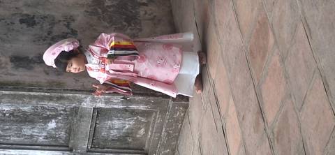Child dressed in traditional attire, standing in a rustic setting.