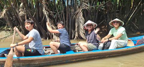 People riding a small boat through a lush, narrow river channel.