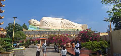 Large statue of a reclining Buddha with several visitors walking around.