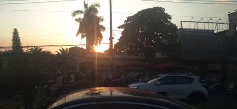 Silhouette of vehicles and motorbikes against a sunset in a busy street setting.