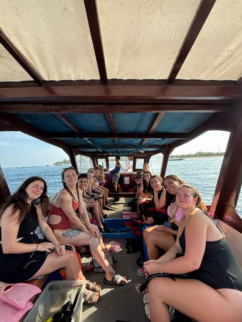 Group of people on a boat smiling towards the camera with water in the background.