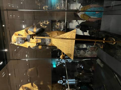 Golden and black wooden pharaoh statue displayed inside a museum glass case with visitors reflected in the background.