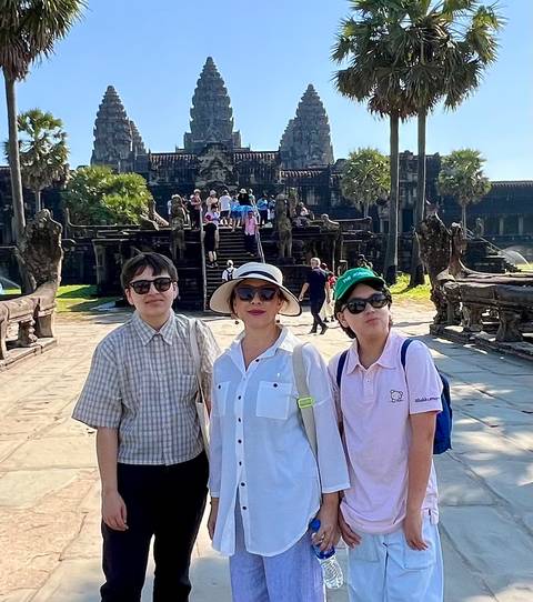 Family posing in front of an ancient ruin with several tourists in the background.