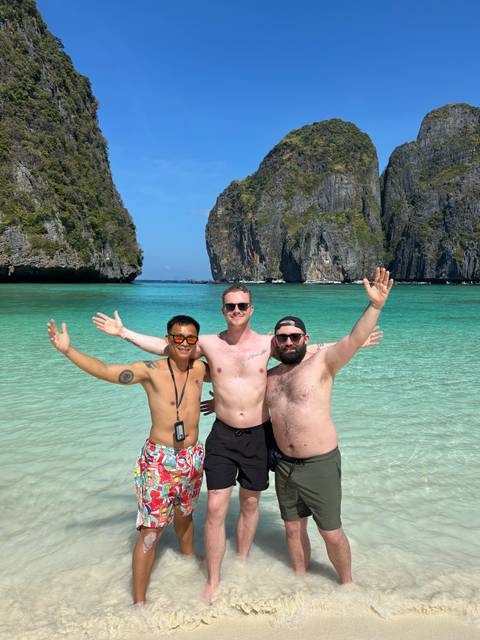 Three friends with arms outstretched in crystal-clear turquoise water between dramatic limestone cliffs on a sunny day.