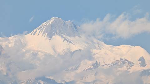 Snow-clad Himalayan summit rising above drifting clouds against a clear blue sky.