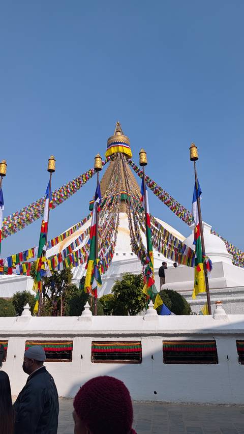 Prayer flags radiate from the towering white Boudhanath stupa as visitors walk below.