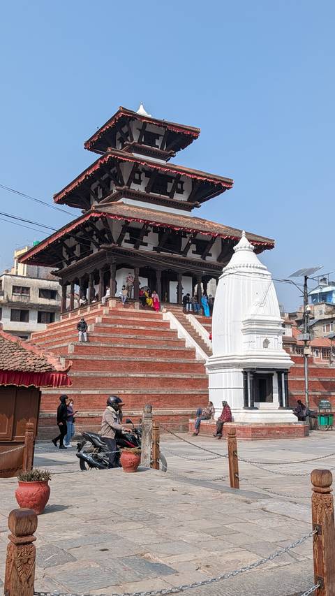 Visitors gathered on the red-brick stepped plinth of a traditional Nepali temple in a busy square.