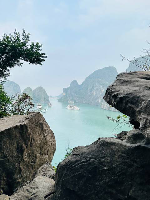 Framed vista of jade-green waters and karst islands of Halong Bay seen between rugged rocks and foliage.