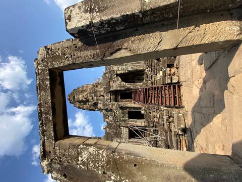 Stone doorway frames steep wooden stairs leading into a Khmer temple ruin against blue sky.