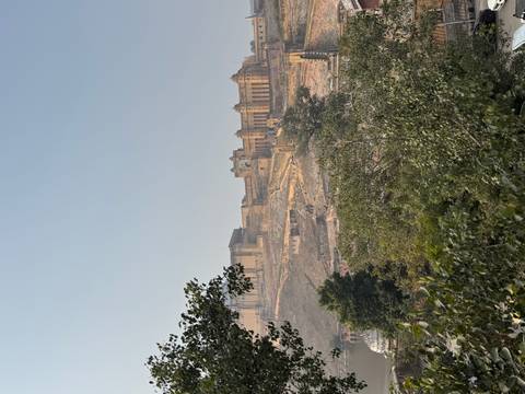 A large hilltop fort of yellow sandstone rising above dry terrain and trees under a clear blue sky.